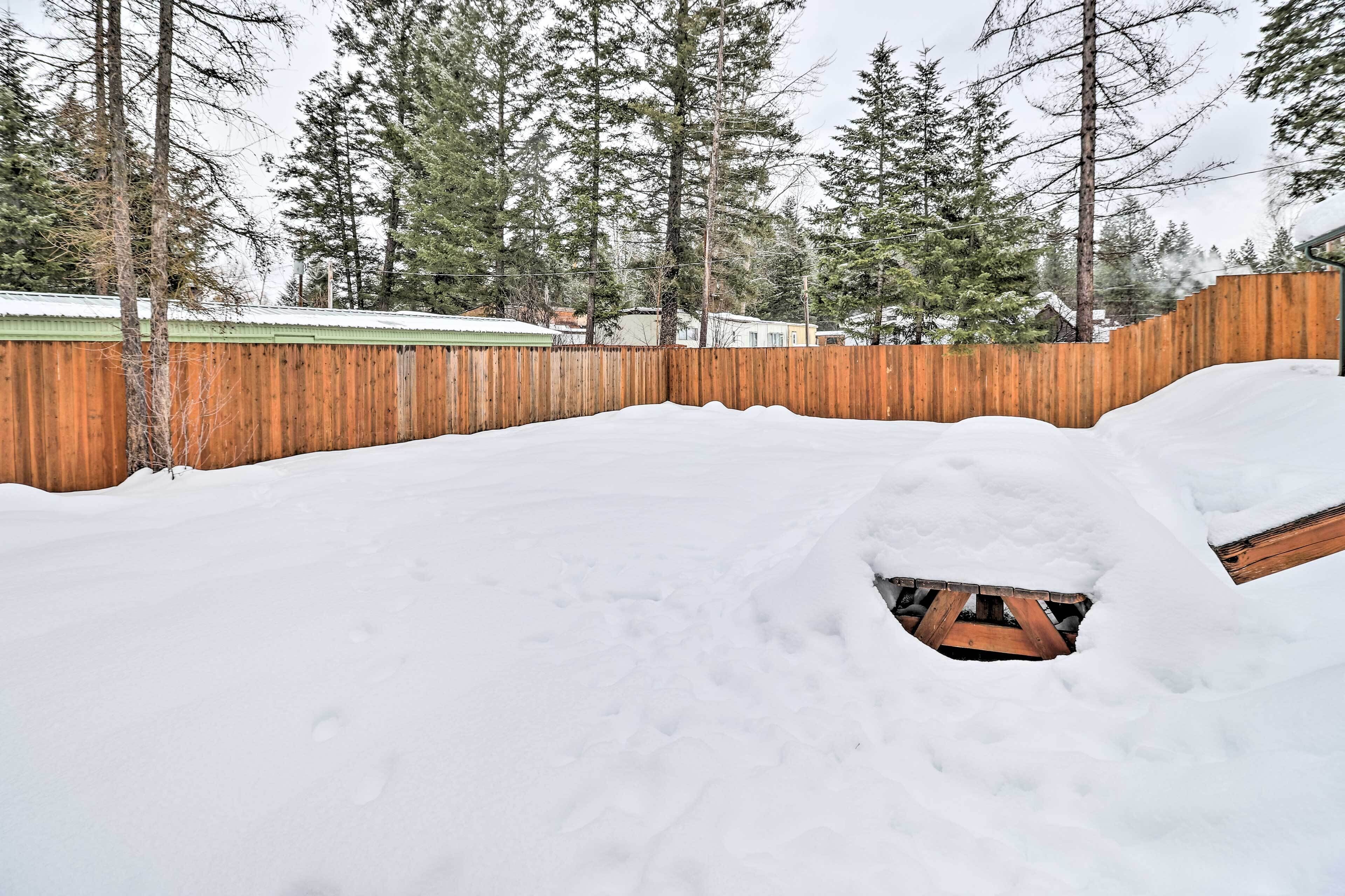Ein schneehoher Garten mit Holzzaun und einer teilweise im Schnee liegenden Holzterrasse.