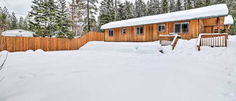 Eine Holzhütte mit schneebedecktem Dach, umgeben von einem Holzzaun und hoch aufragenden Nadelbäumen.