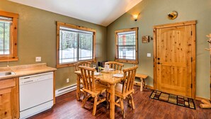 A dining area with a wooden table and chairs, a wooden door, and a window with a view of trees. - Hungry Horse Cabin: 11 Mi to Glacier National Park (Hungry Horse)