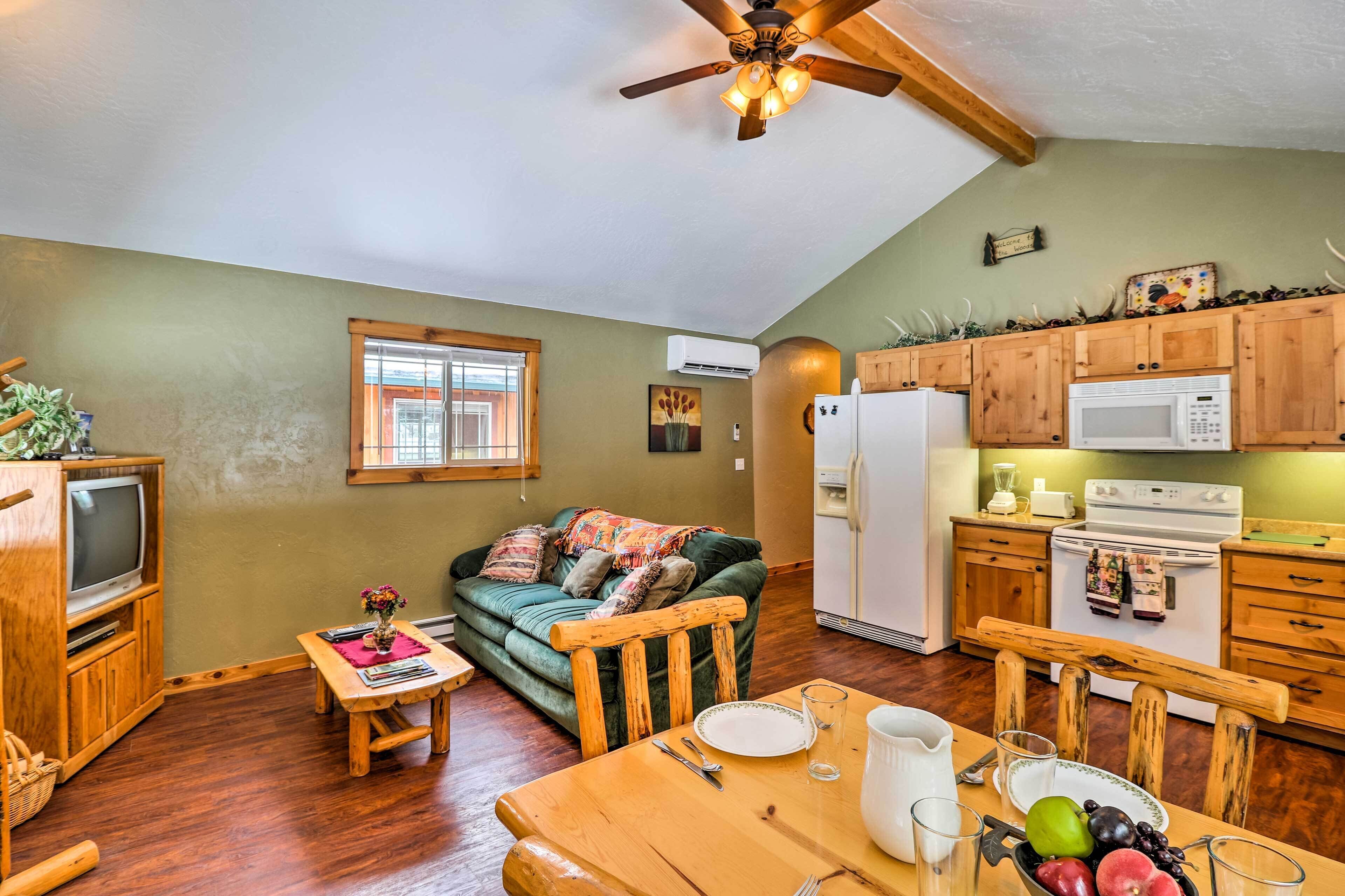 A cozy living room with a wooden TV stand, a green couch, and a dining table set with plates and glasses.