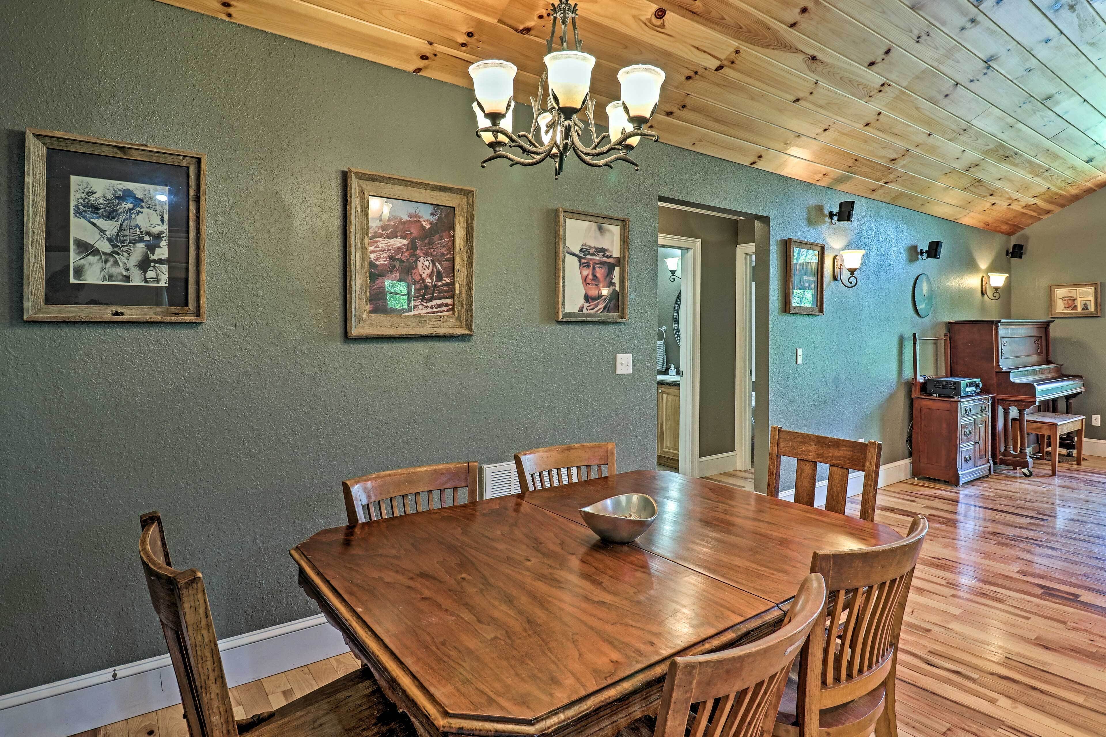 A dining area with a wooden table and chairs, framed pictures on the wall, and a chandelier.