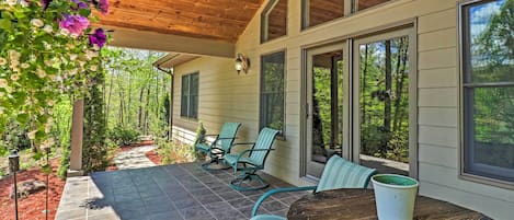 A covered patio with a table and chairs, a hanging flower arrangement, and a view of the surrounding forest.