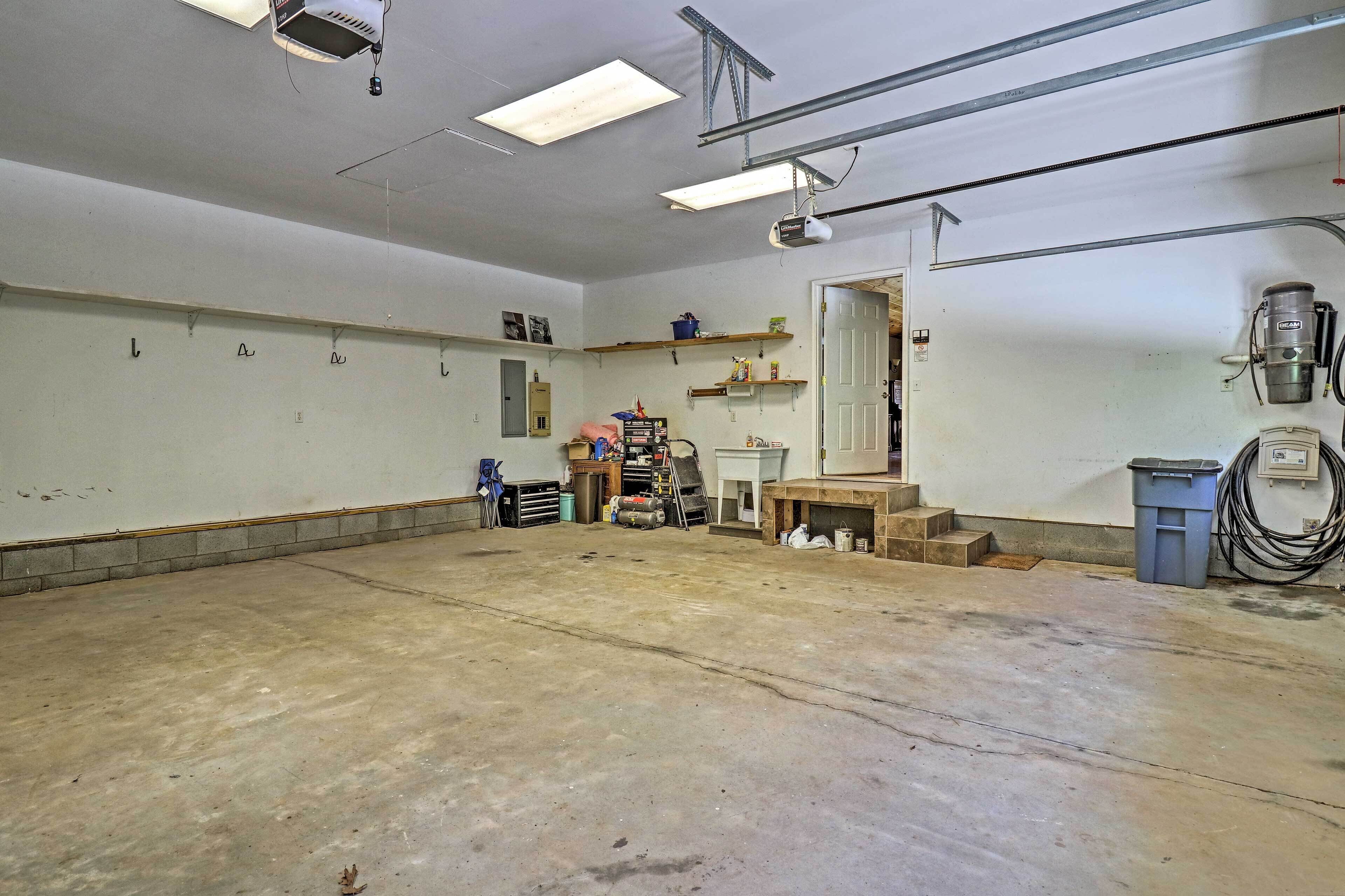 A spacious indoor area with a concrete floor, a door, and various items like a trash bin, a ladder, and shelves with supplies.