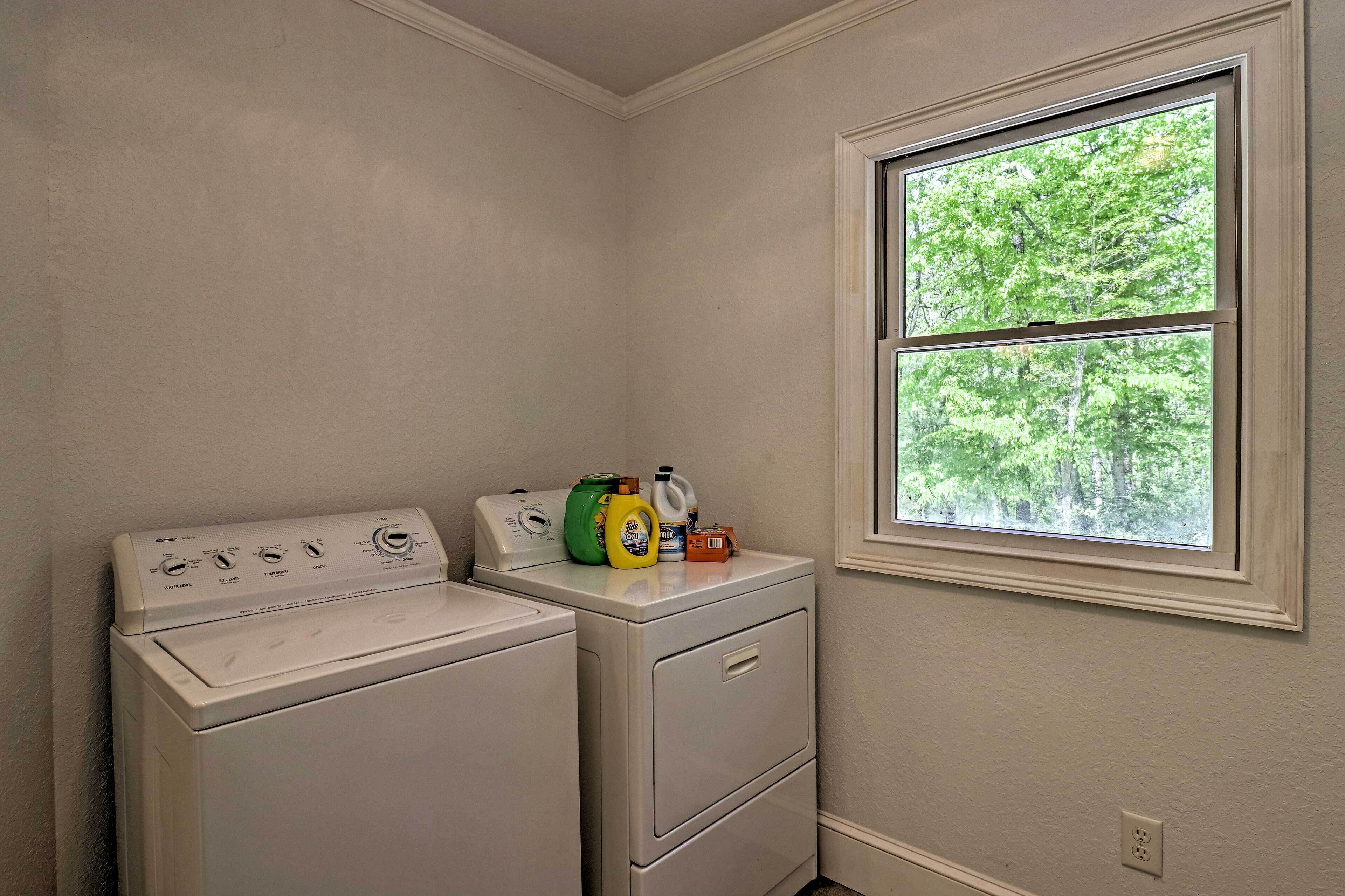 A laundry room with a washer and dryer, a window with a view of trees, and laundry supplies on the dryer.