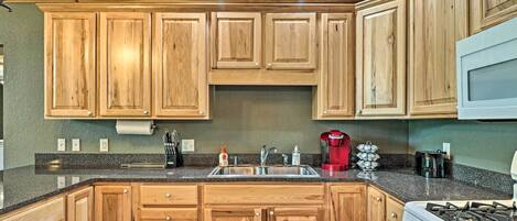 A kitchen with wooden cabinets, a granite countertop, a red coffee maker, and a stove.