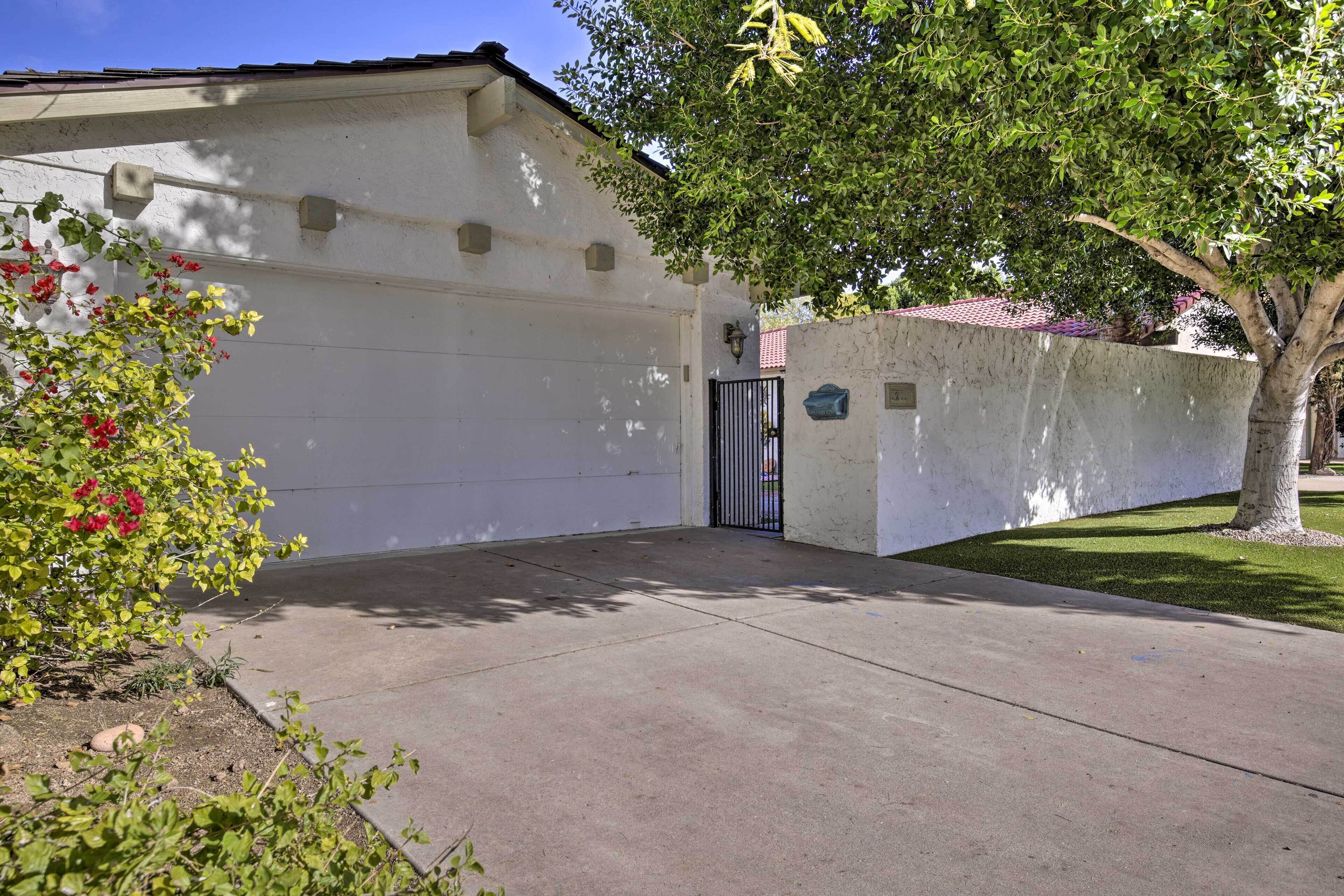 Un garage residenziale con ingresso chiuso da cancello, un muro esterno bianco e un albero che offre ombra.