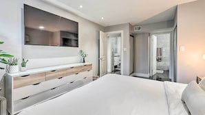 Ein modernes Schlafzimmer mit einem großen Bett, einem an der Wand montierten Fernseher, einem Nachttisch mit Pflanzen und einem begehbaren Kleiderschrank.