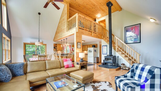 A spacious living area with a high ceiling, wooden beams, a staircase, a fireplace, and a dining area with a view of the outdoors. - Rustic North Creek Getaway ~ 4 Mi to Gore Mtn! (North Creek)