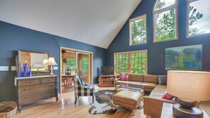 A spacious living room with a high ceiling, wooden flooring, a large window, a sofa, a coffee table, a television, and a fireplace. - Rustic North Creek Getaway ~ 4 Mi to Gore Mtn! (North Creek)