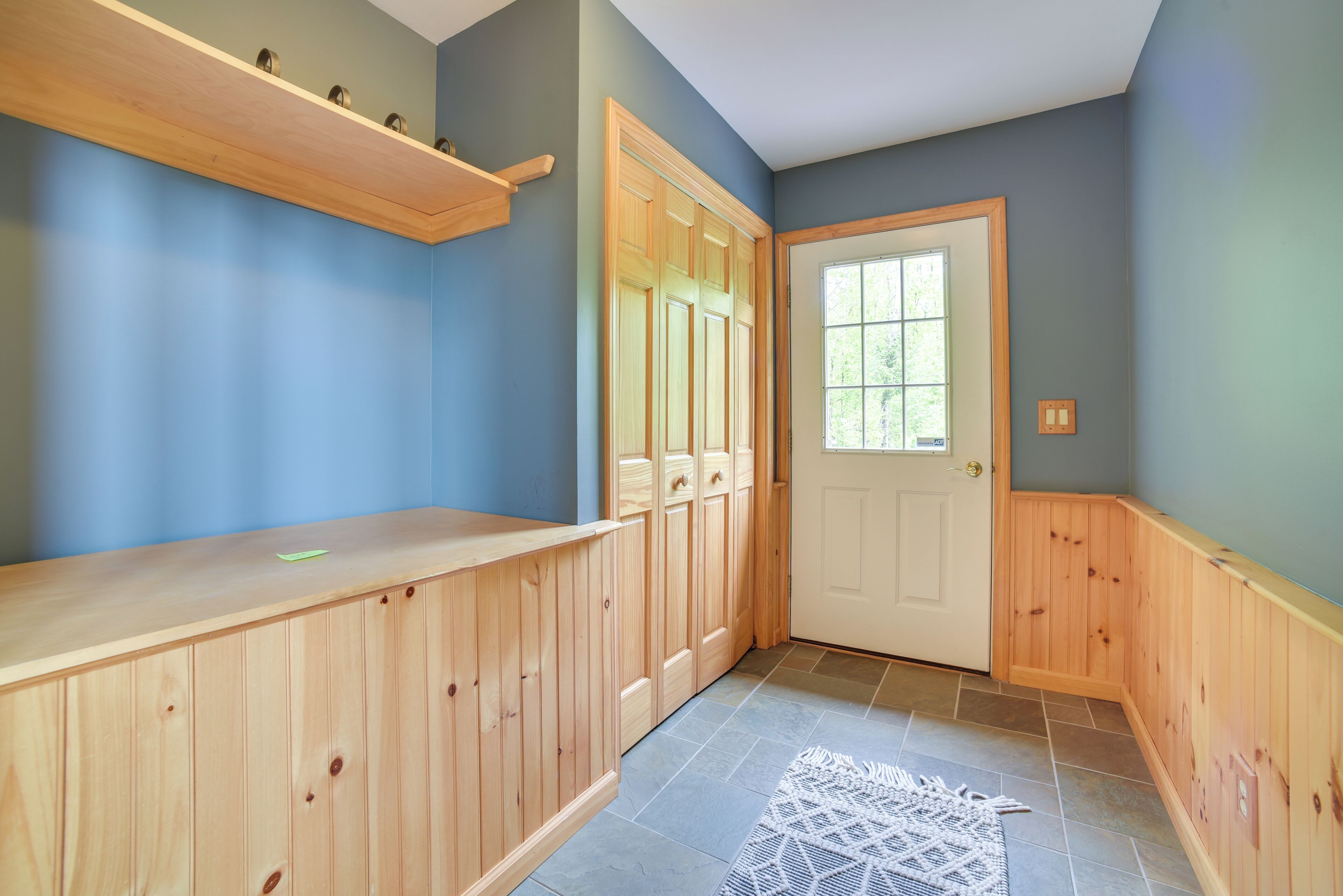 A hallway with wooden paneling, a door with a window, and a tiled floor.