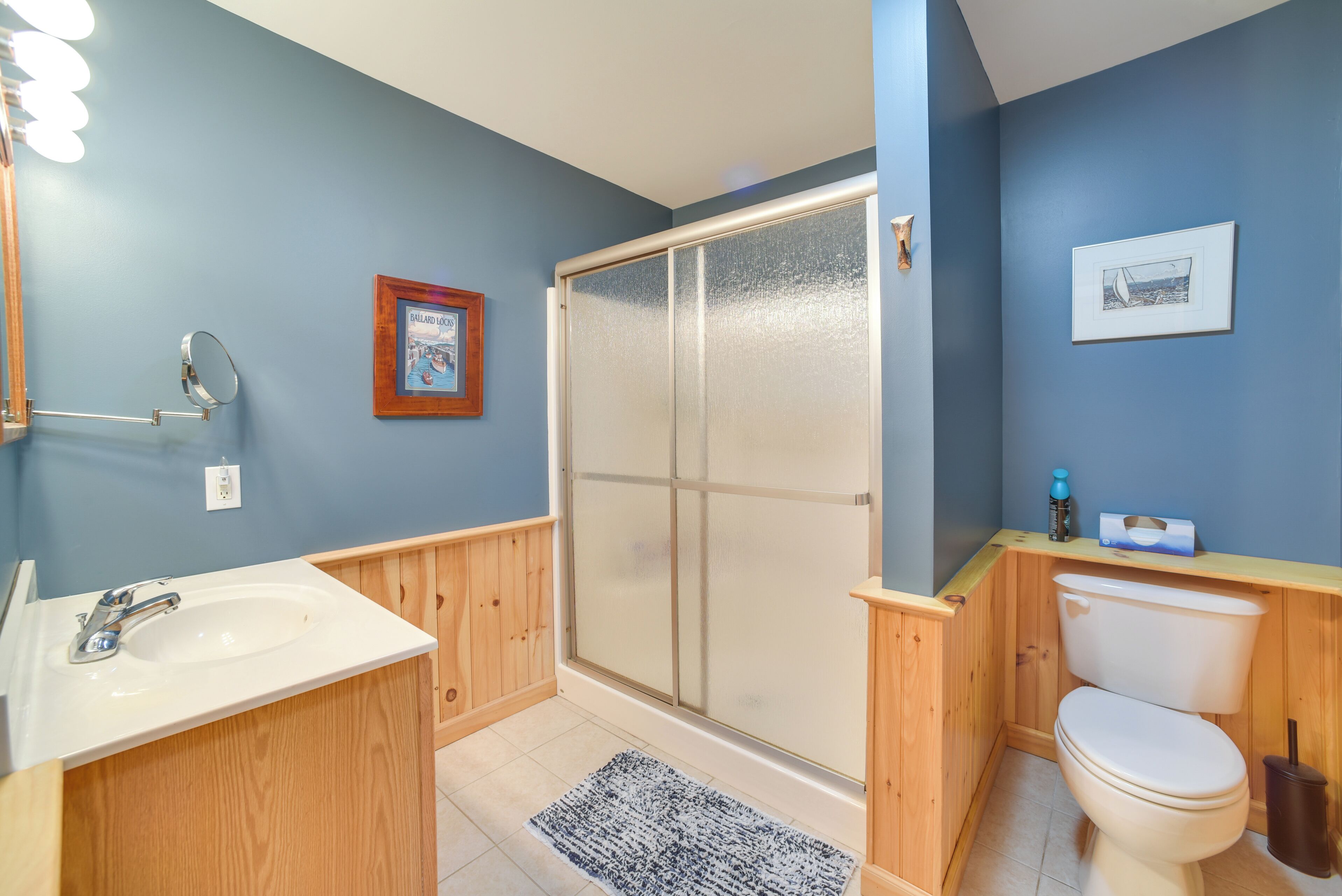 A bathroom with a wooden vanity, a sink, a toilet, and a shower with frosted glass doors.
