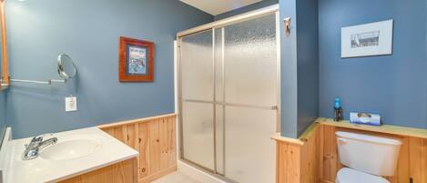A bathroom with a wooden vanity, a sink, a toilet, and a shower with frosted glass doors.