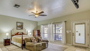 A bedroom with a bed, a wooden nightstand, a dresser, a sofa, a ceiling fan, and a large window with curtains. - Pool & Game Room: Waterfront Harlingen Home (Harlingen)