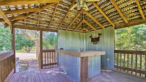 A covered outdoor area with a wooden deck, a metal railing, and a corrugated metal wall. - Pool & Game Room: Waterfront Harlingen Home (Harlingen)