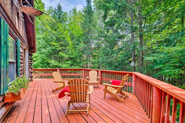 A wooden deck with Adirondack chairs and a red railing, surrounded by dense green forest.