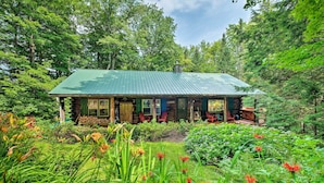 A log cabin with a green metal roof, surrounded by lush greenery and flowering plants. - Private Wooded Cabin: 7 Mi to Mount Snow! (Wilmington)