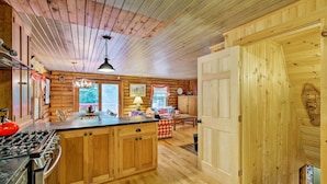 A wooden cabin interior with a kitchen featuring a stove, cabinets, and a dining area with a table and chairs. - Private Wooded Cabin: 7 Mi to Mount Snow! (Wilmington)
