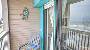Un balcon avec une chaise, une figurine de lézard décorative et une vue sur l’océan, visible à travers une porte vitrée.