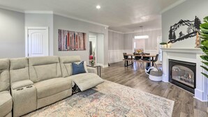 A living room with a beige sofa, a patterned rug, a fireplace, and a dining area with a table and chairs.