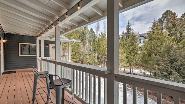 A covered deck with wooden flooring and metal chairs, overlooking a snowy landscape and trees.