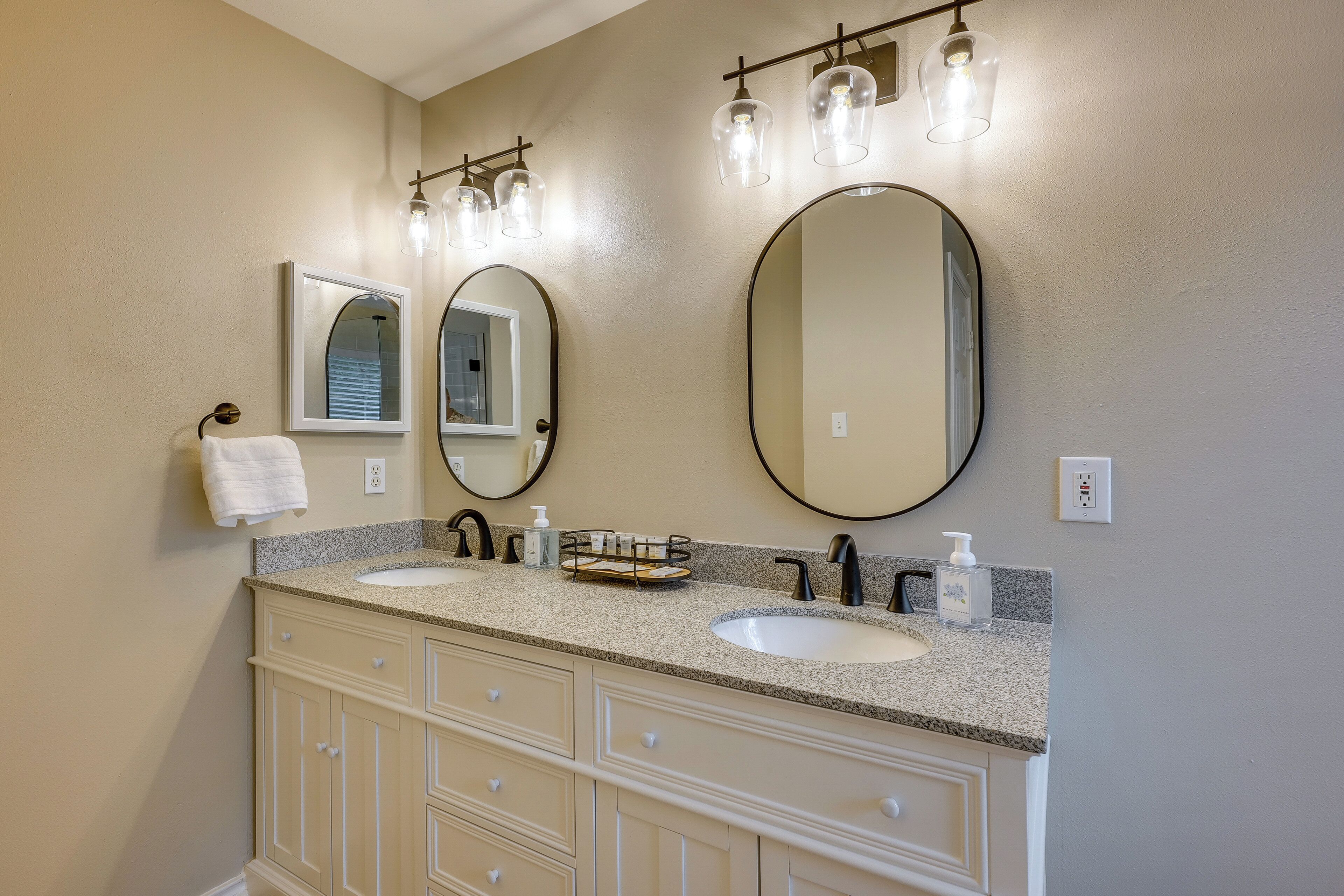 A bathroom with two sinks, a vanity with drawers, a mirror, and a towel rack.