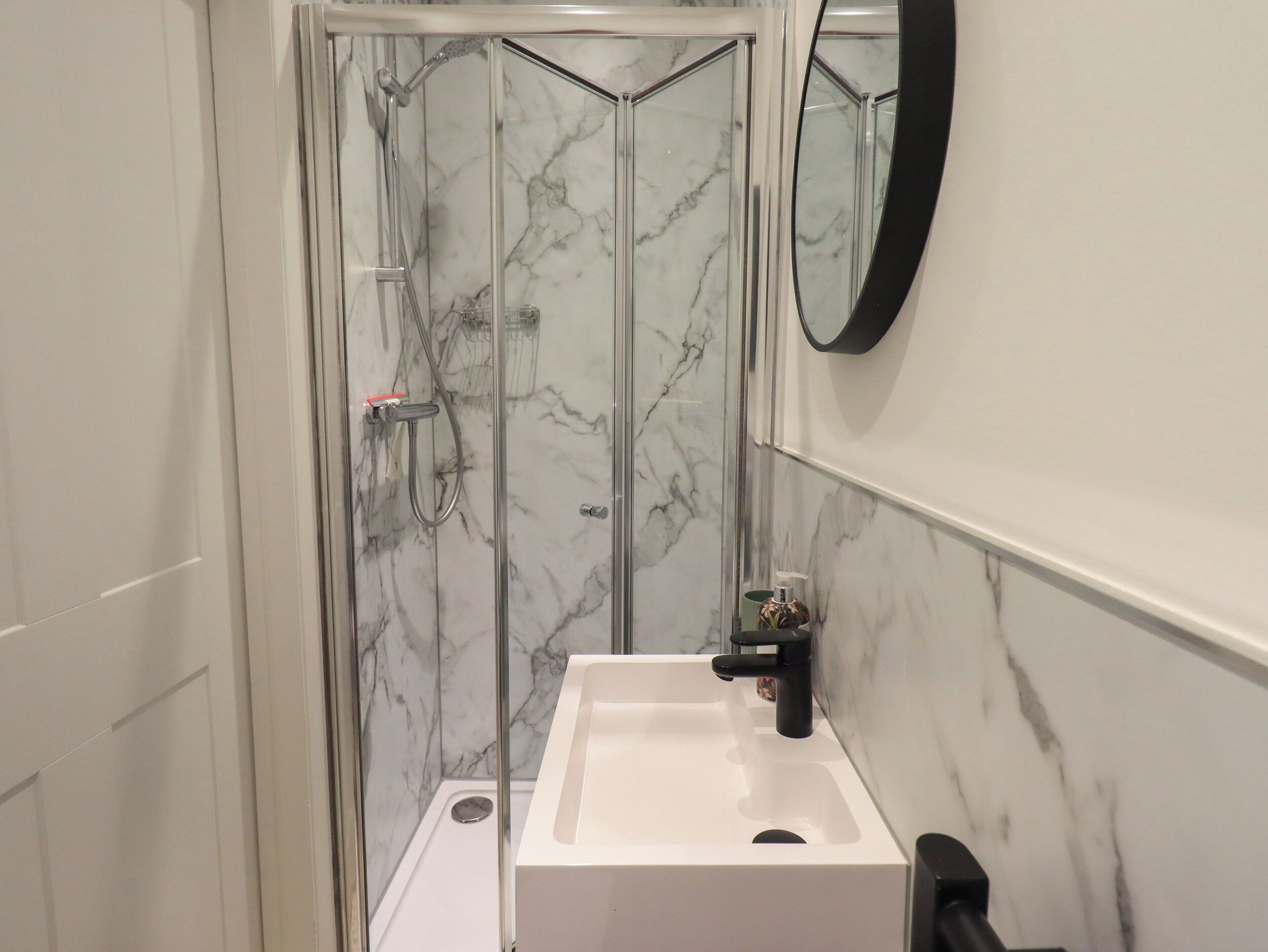 A bathroom with a glass-enclosed shower, a white sink, and a marble-tiled wall.