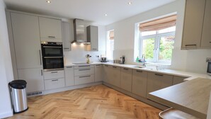 A modern kitchen with white cabinets, a stainless steel range hood, and a herringbone wood floor. - Limhus House (Keswick)