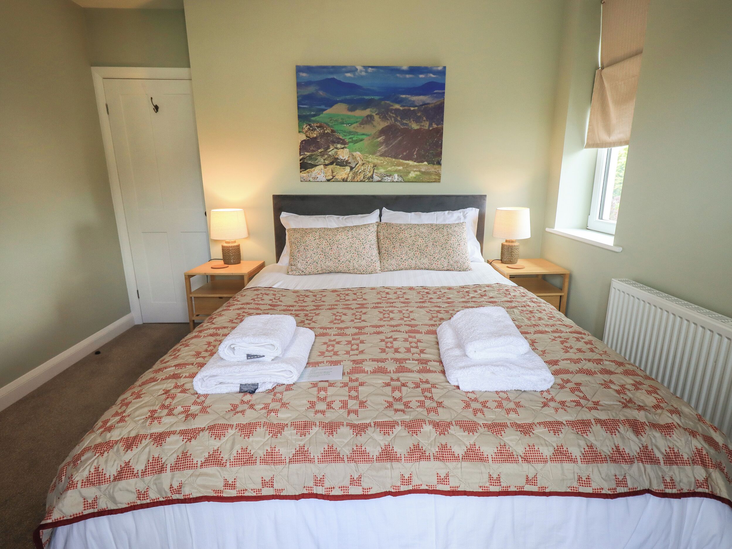 A neatly made bed with a patterned bedspread, two pillows, and two folded towels on the bed.