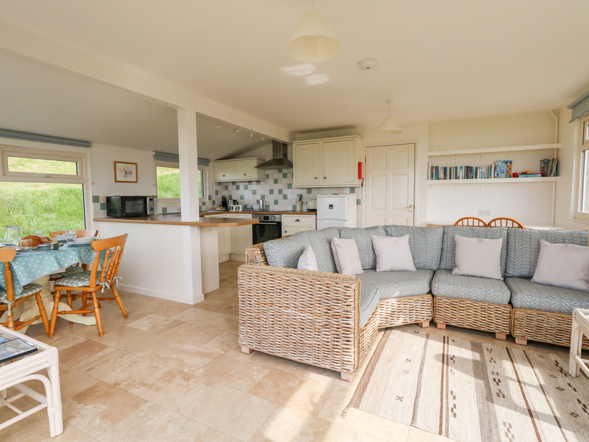 Una sala acogedora con sofá, sillas, una mesa de comedor y una cocina con armarios blancos y un salpicadero de azulejos.