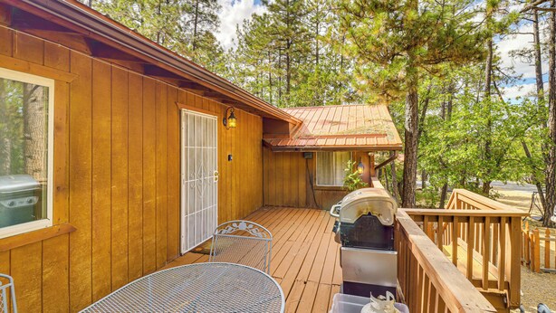 Una cabaña de madera con terraza, una mesa de metal y una parrilla.