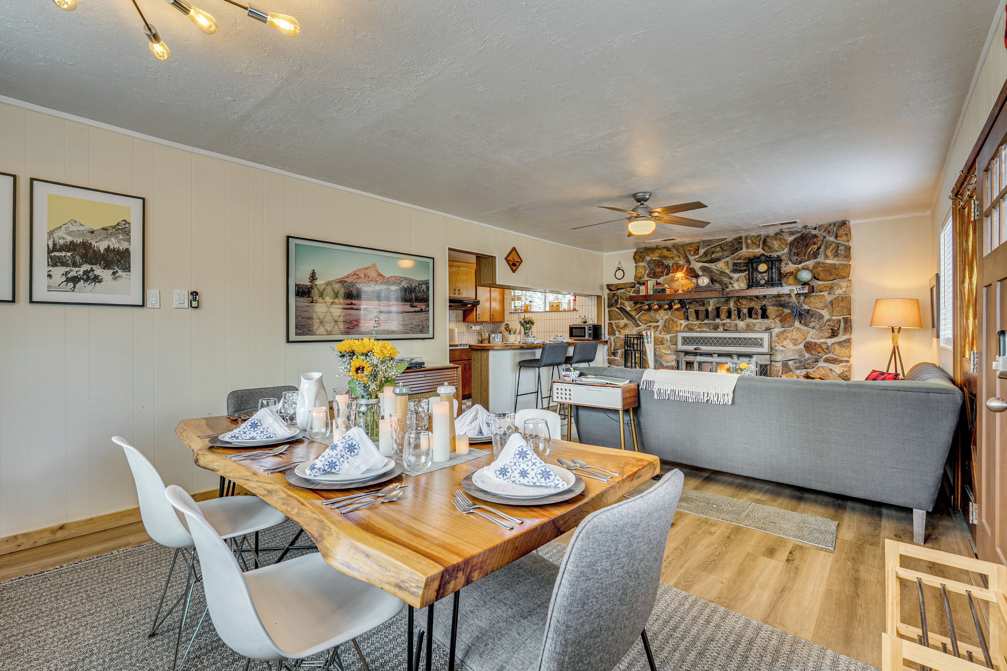 A dining area with a wooden table set for four, white chairs, and a grey sofa in the background.