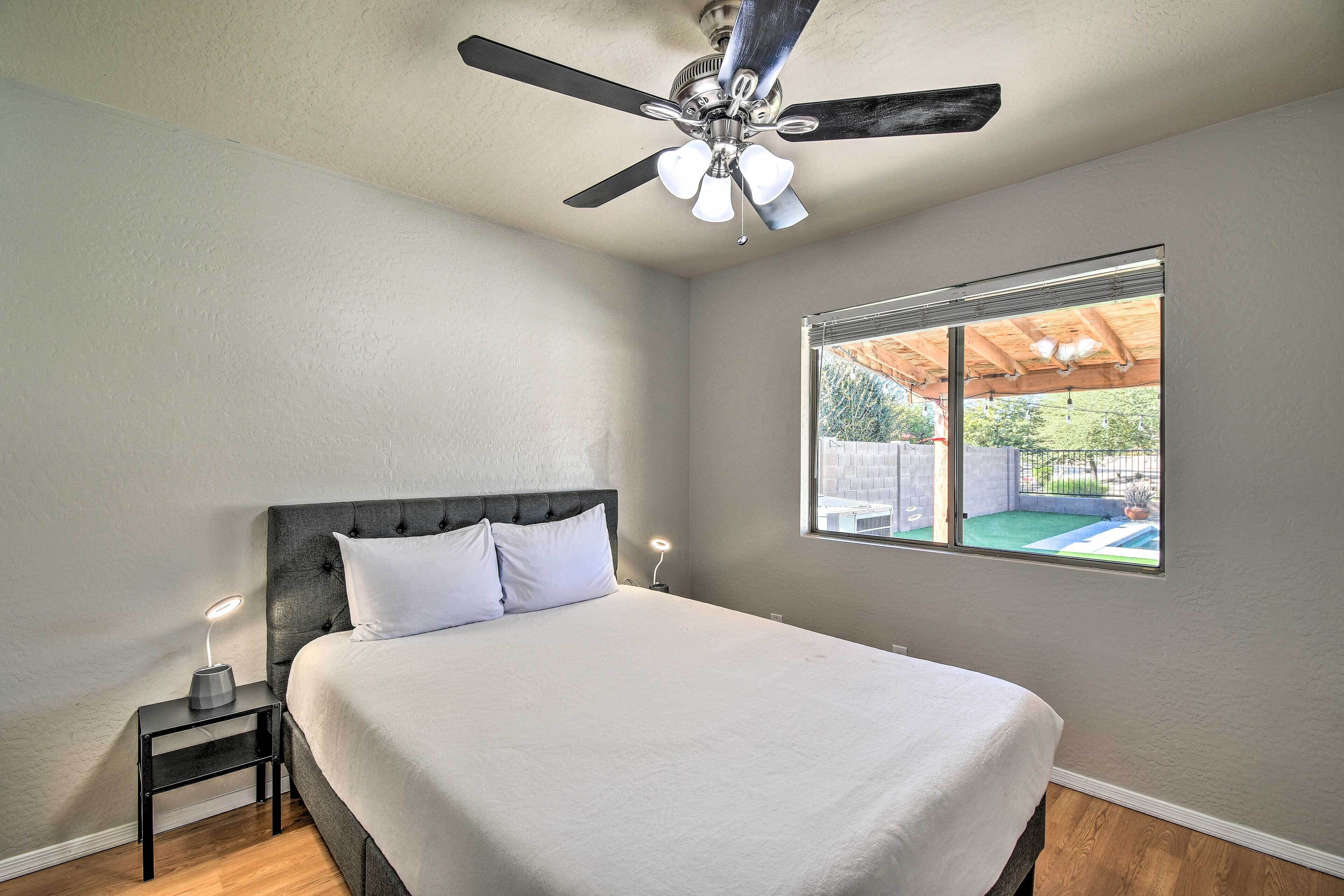 A bedroom with a bed, a nightstand with a lamp, a ceiling fan, and a window with a view of an outdoor area.