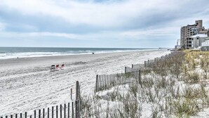 A beach with a wooden fence, beach chairs, and a building in the background.