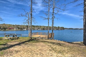 A lakeside park with a wooden deck, picnic tables, and a view of a lake with buildings in the background. - 3 Mi to Lake Desoto: Home w/ Furnished Deck! (Hot Springs Village)