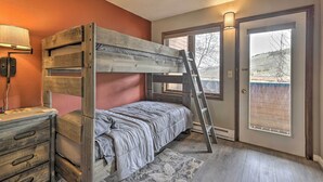 Ein Stockbett mit einer Leiter, ein Schreibtisch mit Schubladen, eine Lampe und ein Fenster mit Blick auf eine verschneite Landschaft.