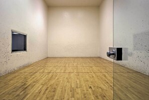 Une pièce spacieuse avec un plancher en bois, une petite fenêtre et une porte dotée d’une poignée.