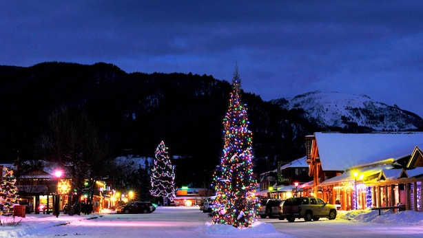 A snowy town square with Christmas trees and illuminated buildings.