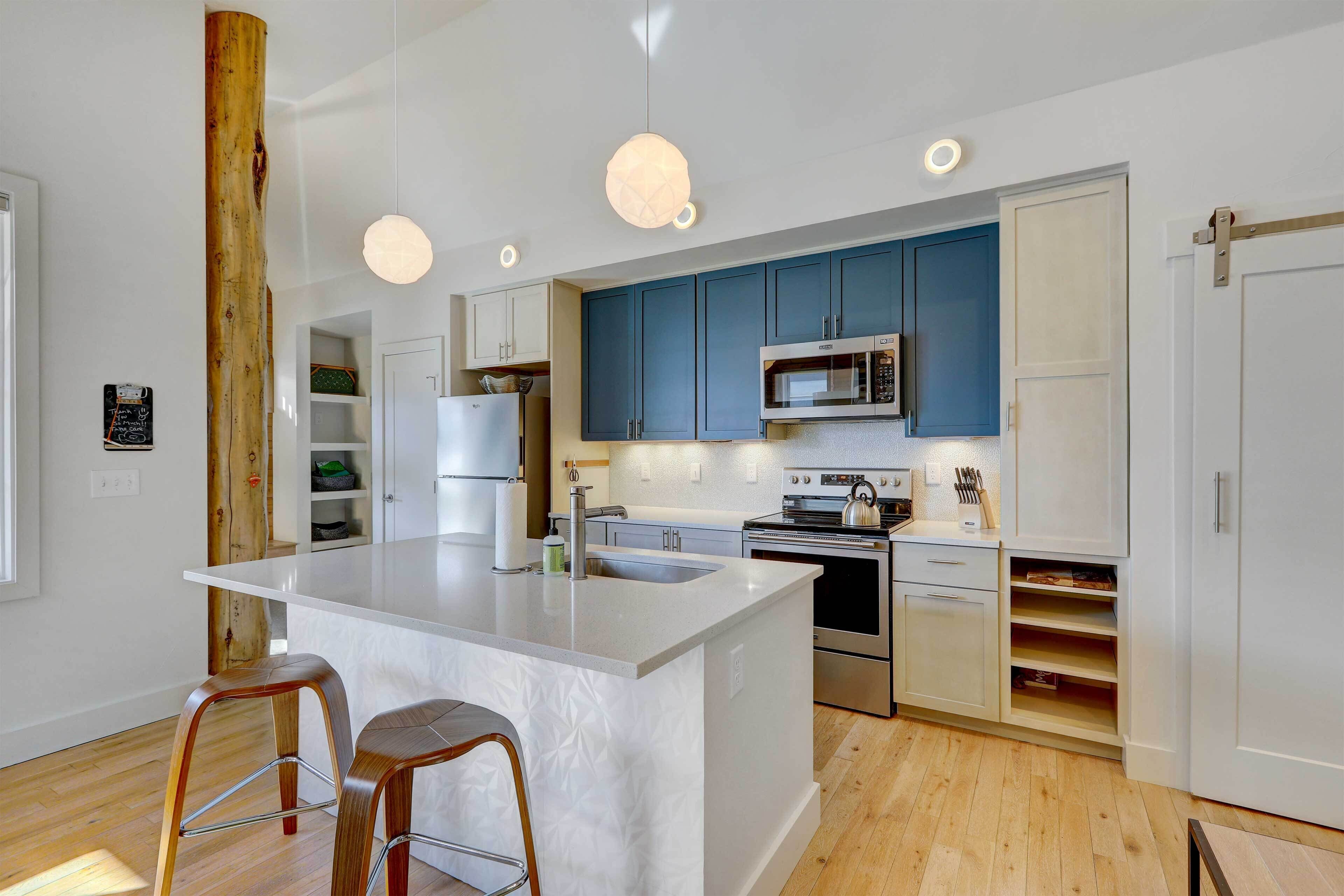 A modern kitchen with a central island, stainless steel appliances, and blue cabinets.