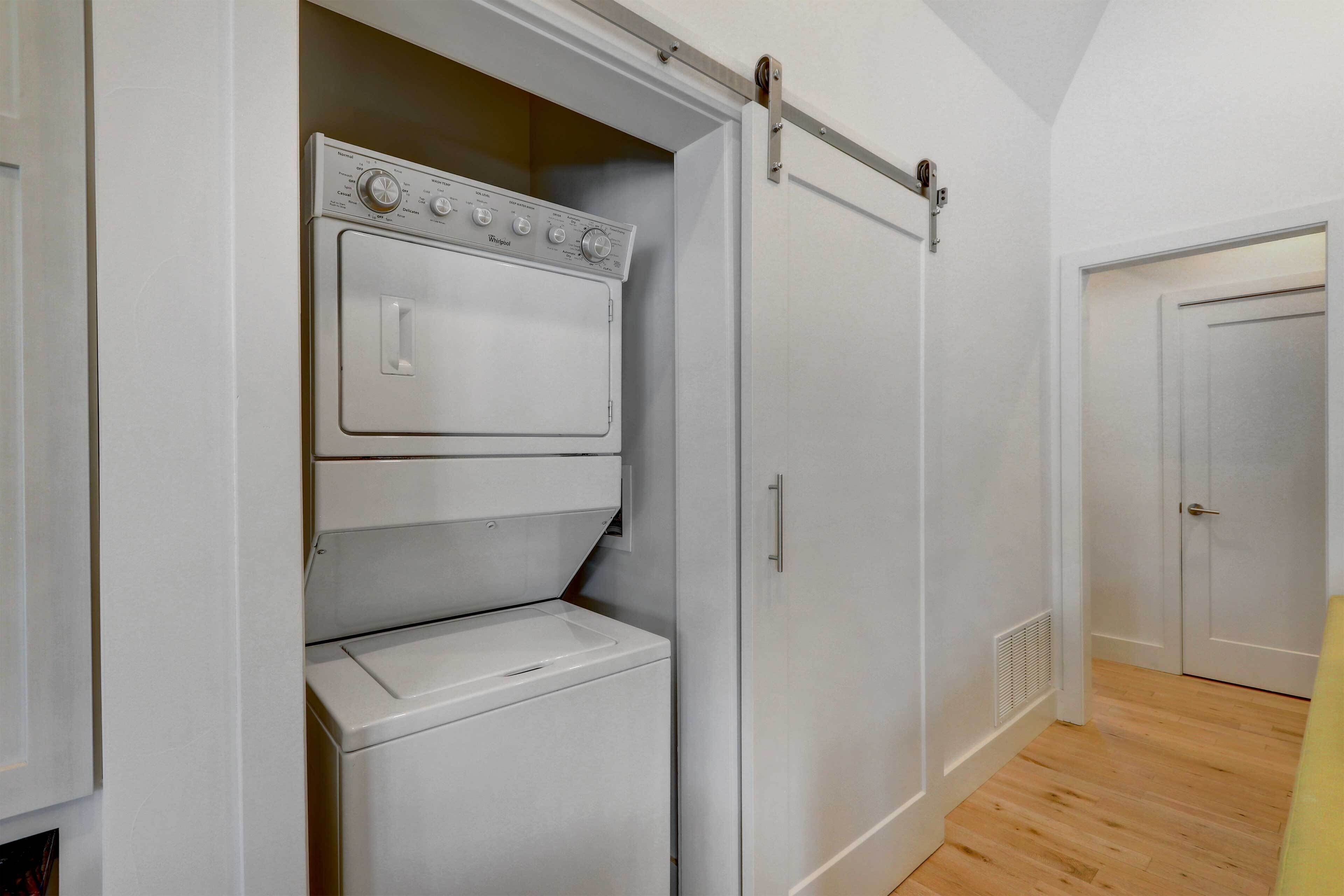 A laundry room with a front-loading washer and dryer, a sliding door closet, and a wooden floor.