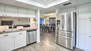 A modern kitchen with white cabinets, stainless steel appliances, and a dining area with dark chairs and a table. - Movie Room & Private Pool: Richardson Retreat (Richardson)