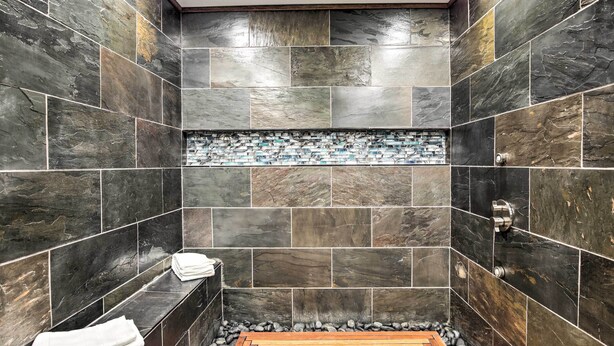 A bathroom with dark stone tiles, a wooden bench, and a tiled shower area. - Movie Room & Private Pool: Richardson Retreat (Richardson)