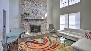 A modern living room with a stone fireplace, a glass coffee table, a white sofa, and a colorful rug. - Movie Room & Private Pool: Richardson Retreat (Richardson)