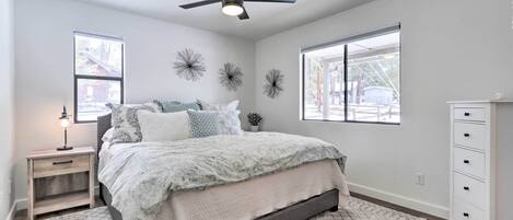 Un dormitorio con cama, mesita de noche, cómoda, ventilador de techo y decoración mural.