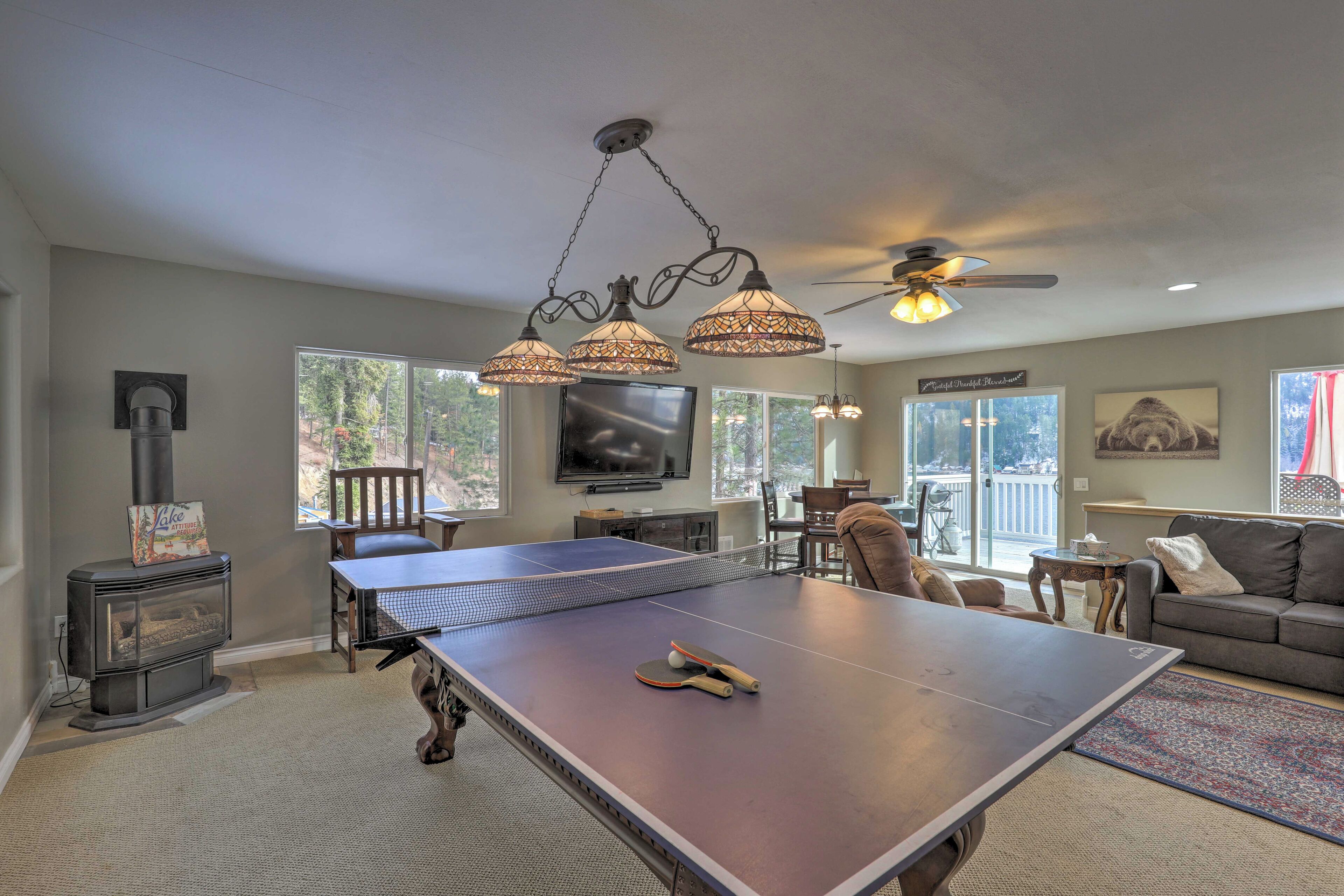 Una sala de estar con mesa de ping pong, chimenea, ventilador de techo y un gran ventanal.