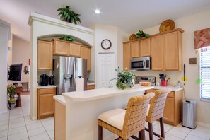 A modern kitchen with wooden cabinets, a stainless steel refrigerator, a microwave, and a large island with two wicker chairs. - Sunny Villa w/ Lanai: 17 Mi to Disney! (Davenport)