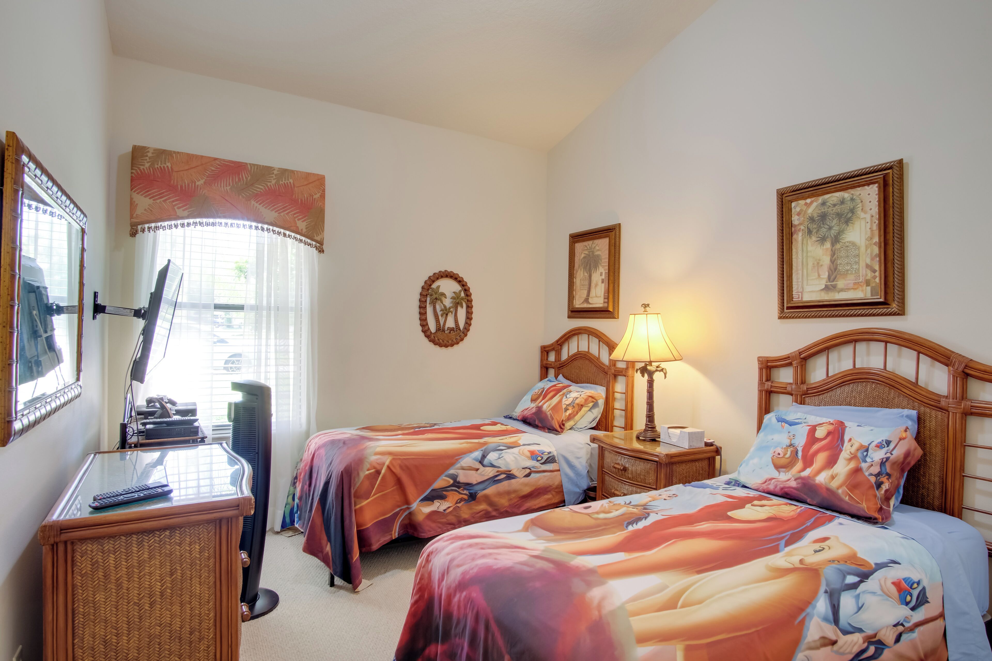 A hotel room with two beds, a desk with a computer, a standing fan, and a window with curtains.