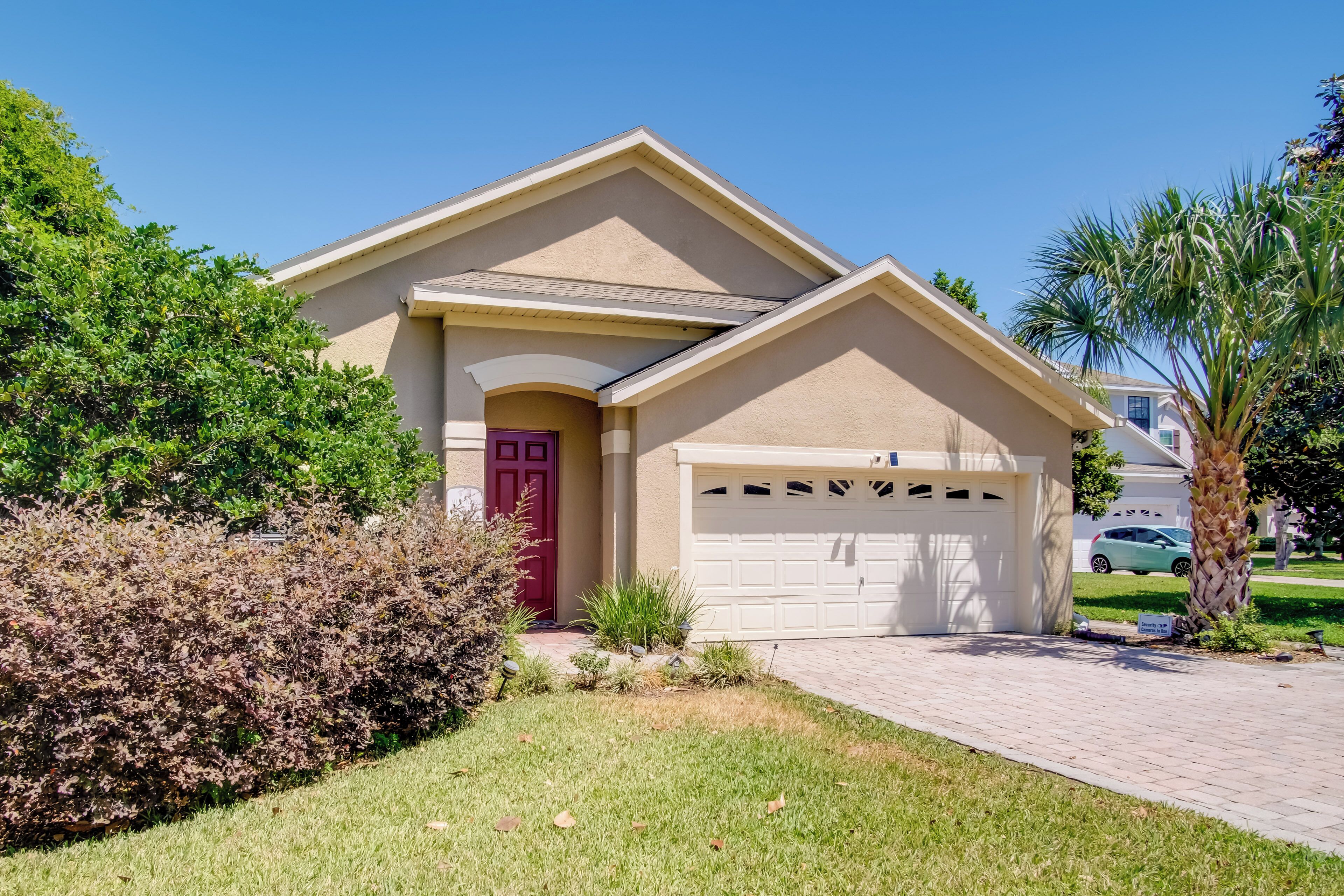 A residential house with a red door, beige exterior, and a white garage door.