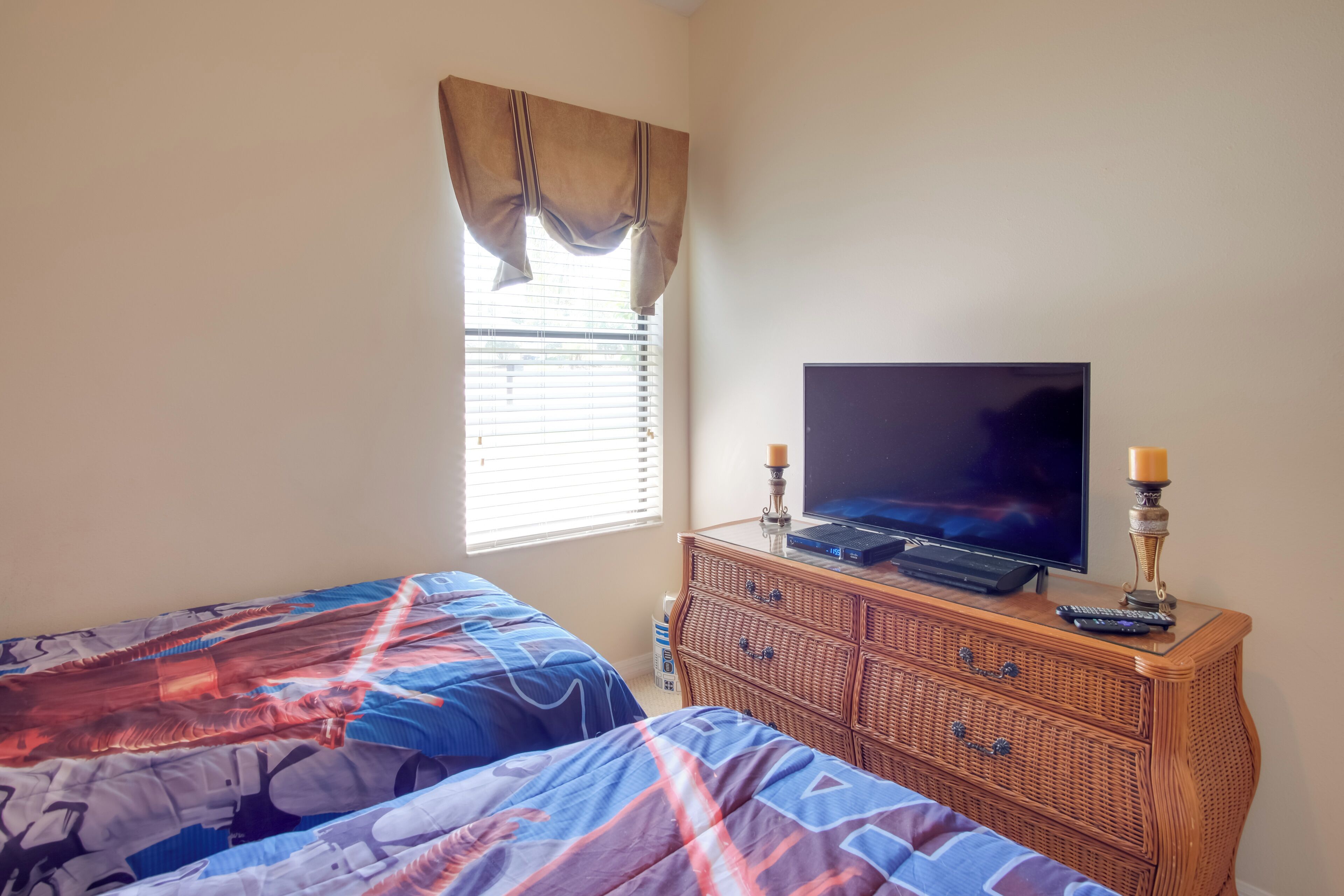 A bedroom with two beds, a television on a dresser, and a window with blinds.