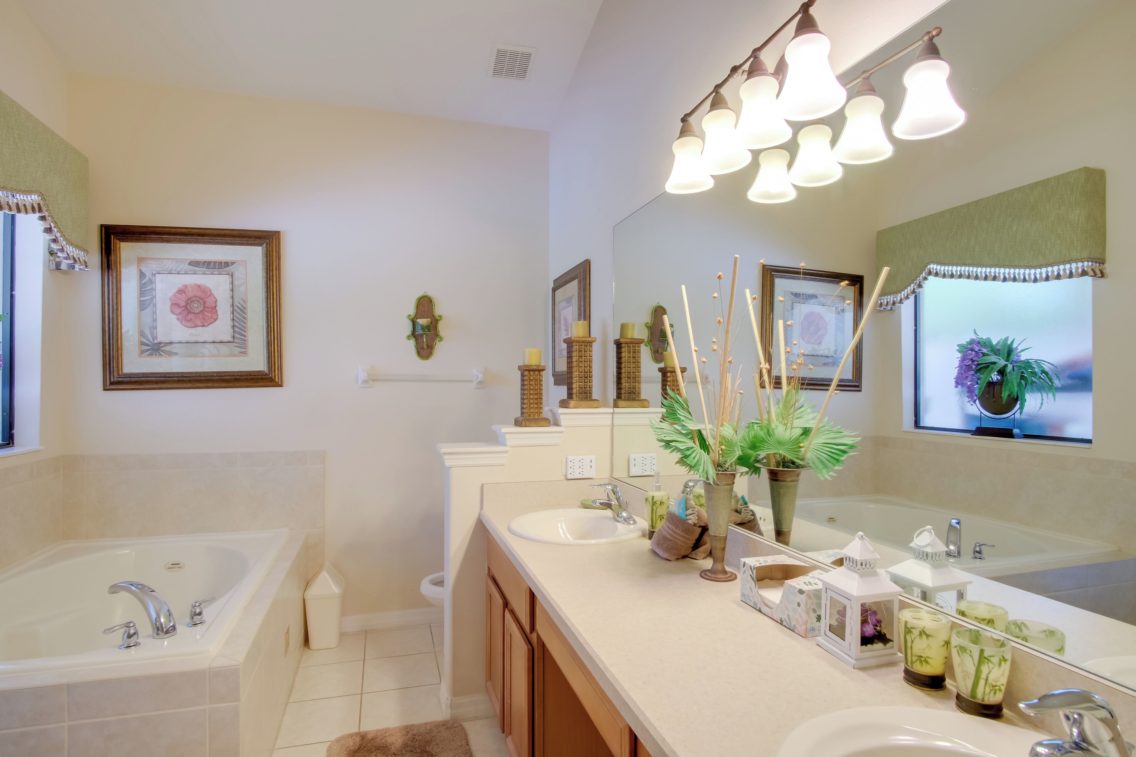 A modern bathroom with a large bathtub, two sinks, and a vanity. There are decorative items like candles and a plant on the vanity.