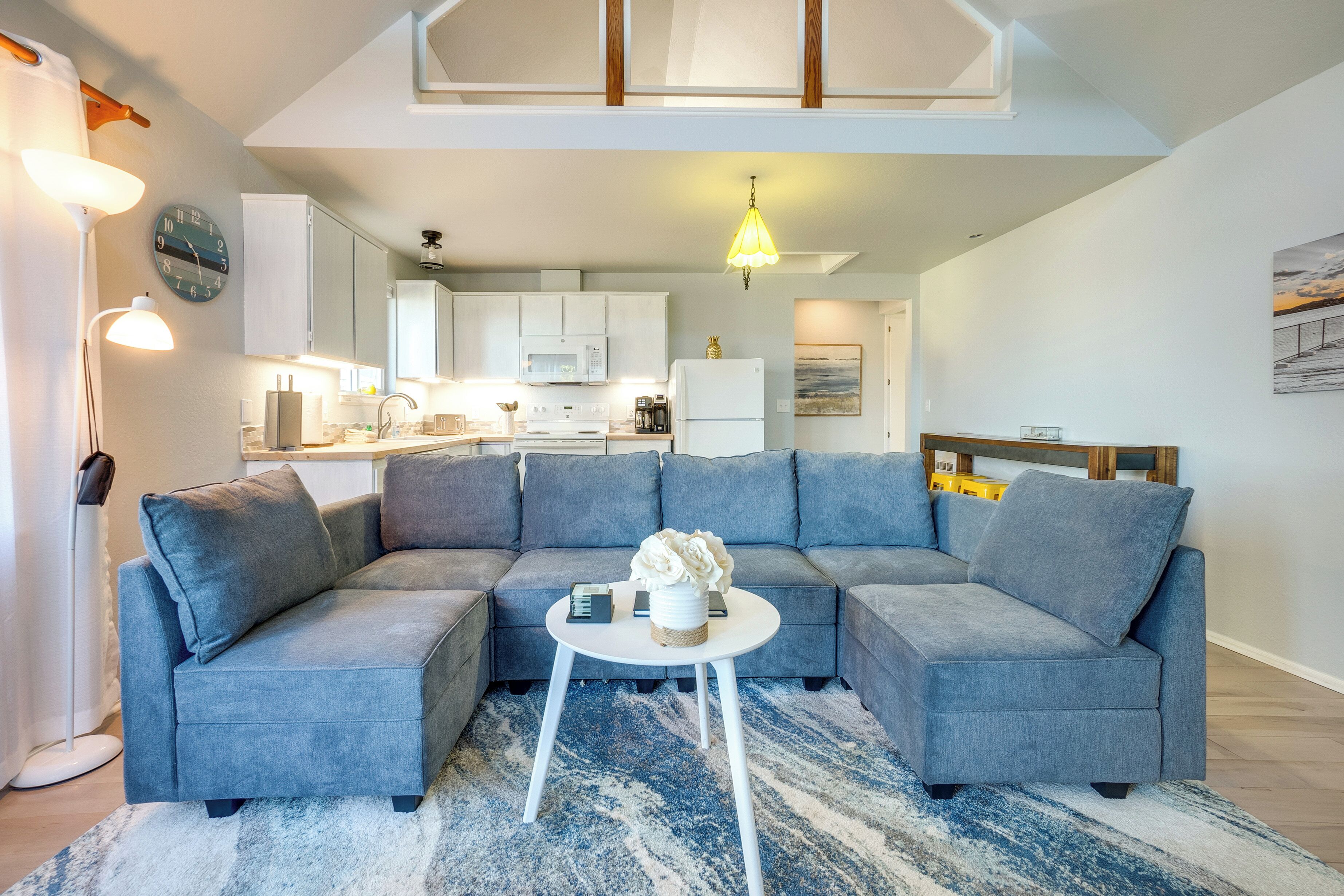 A modern living room with a grey sectional sofa, a round coffee table, and a kitchen in the background.